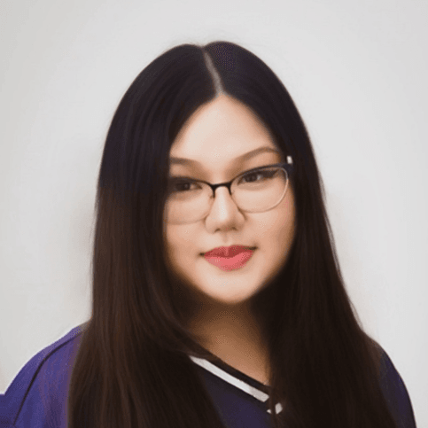 Portrait of a woman with long dark hair and glasses, smiling at the camera, light background.