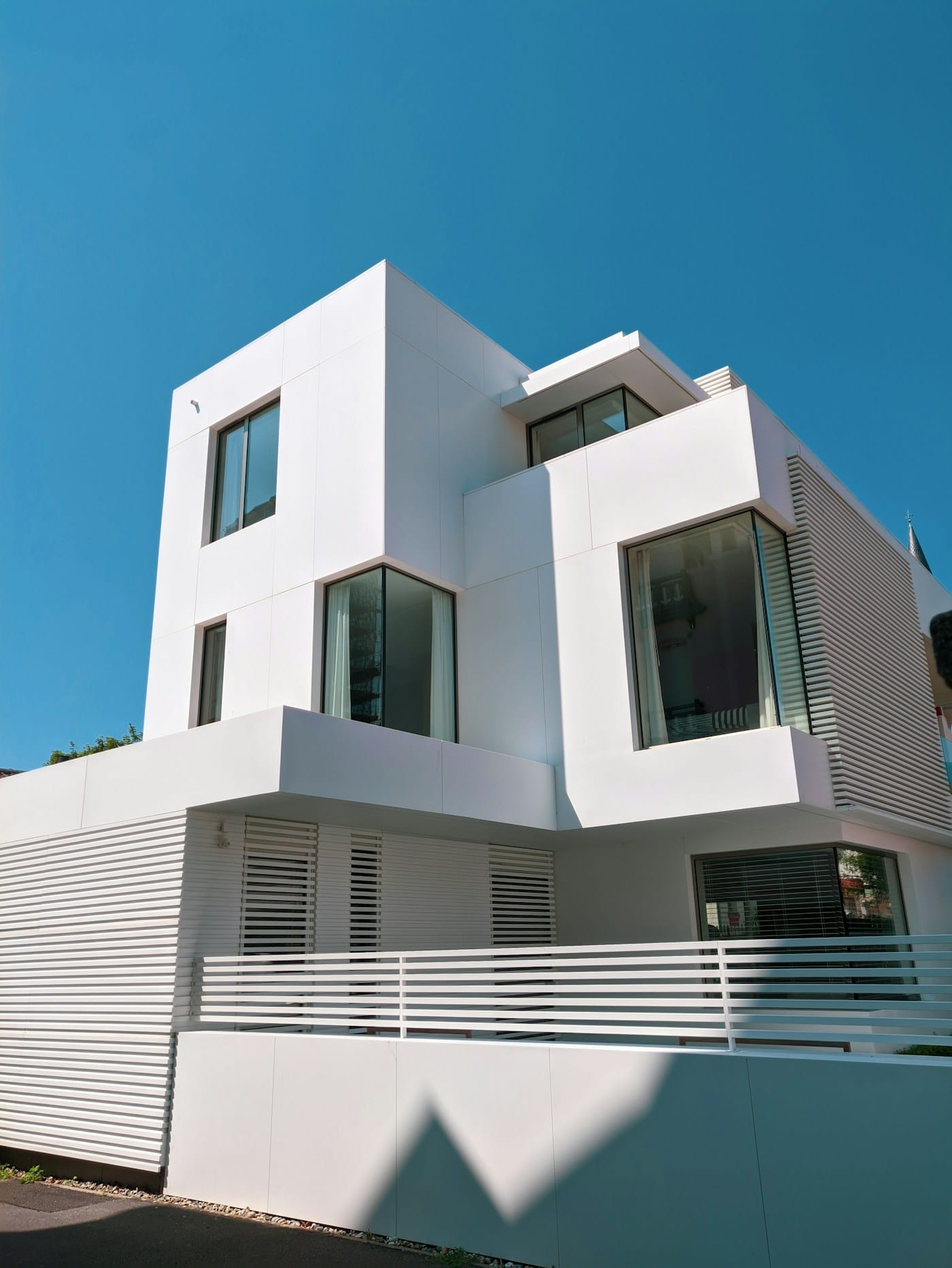 White modern multi-story building with large windows and angular design against a bright blue sky.