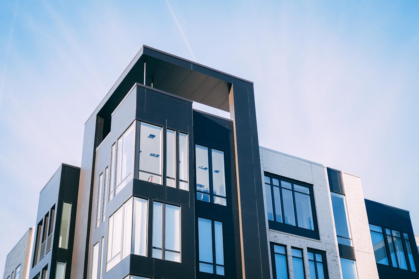Modern multi-story office building with dark panels and large glass windows against a clear blue sky.